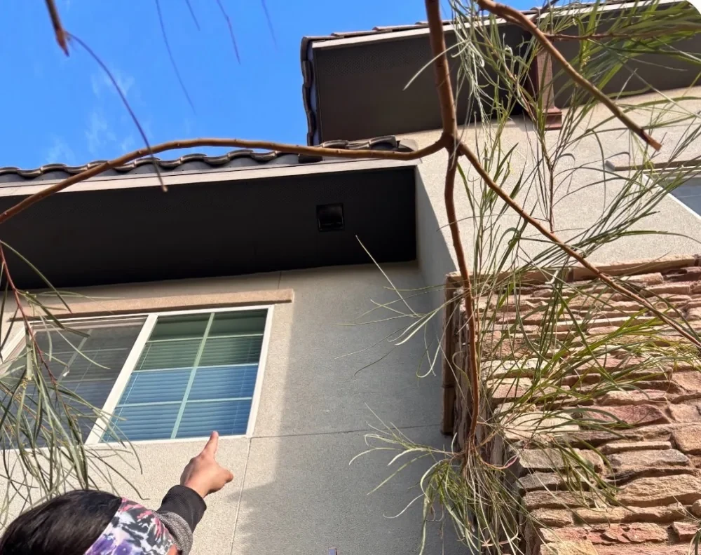 Pointing up at a dryer vent outlet high on a stucco wall under the soffit